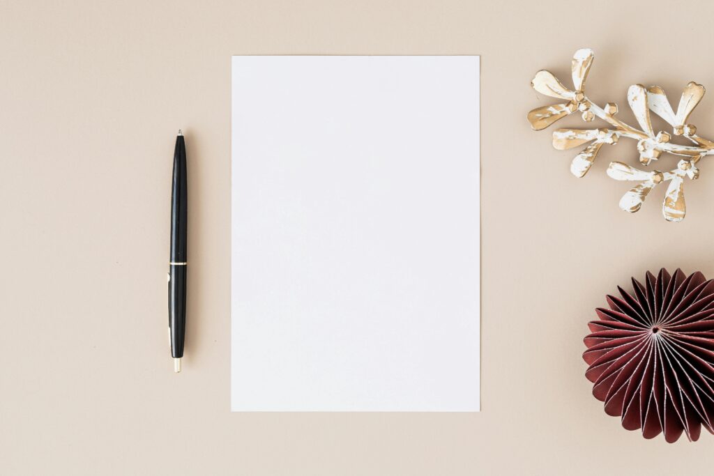 Papier Elegant flatlay with blank paper, black pen, and decorative elements on beige.